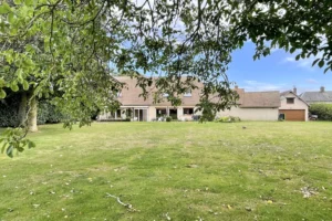 Grand jardin arboré de la maison à vendre à Moisville dans l’Eure, vue depuis les arbres vers la façade arrière et la véranda