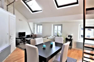 Séjour et salle à manger lumineux du loft à Paris 9 Notre-Dame-de-Lorette, avec grandes fenêtres, poutres apparentes et parquet bois.