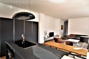 Cuisine ouverte du loft à Paris 11 Parmentier avec îlot central noir, hotte design suspendue et vue sur le salon.