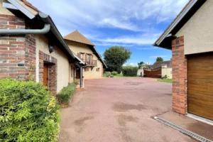 Entrée de la propriété à vendre à Moisville dans l’Eure avec cour pavée, portail en bois et façade en briques