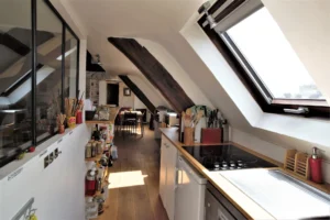 Cuisine aménagée sous combles avec rangements, poutres apparentes et verrière, vue sur l’espace repas, appartement rue de Turenne Paris 3ᵉ.