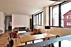 Salon lumineux du loft à Paris 11 Parmentier avec grandes fenêtres, parquet en bois et mobilier contemporain.