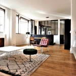 Salon du loft à Paris 11 Parmentier avec parquet en bois, fauteuil design et verrière atelier en arrière-plan.