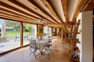 Salle à manger lumineuse de la maison à vendre à Moisville dans l’Eure avec poutres apparentes et grandes baies vitrées sur le jardin