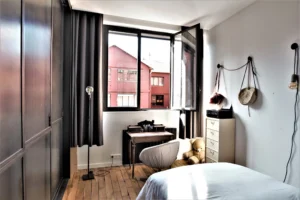 Chambre lumineuse du loft à Paris 11 Parmentier avec parquet, bureau ancien et grande fenêtre.