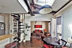 Salon lumineux d’un loft à vendre à Paris 18, Marché de l’Olive, avec poutres apparentes, escalier en colimaçon et décoration contemporaine.