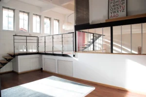 Espace lumineux d’un loft à Paris 19, situé Villa Marcel Lods, avec mezzanine vitrée, escalier contemporain et grandes fenêtres laissant entrer la lumière naturelle.