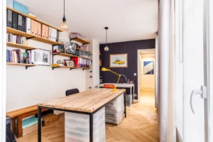 Bureau lumineux avec parquet en chevron, murs contrastés et étagères murales en bois, appartement Paris 10 – Gare de l’Est.