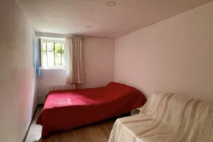 Chambre avec lit double et petite fenêtre donnant sur le parc du château de Villers-sur-Mer, décorée avec sobriété dans des tons clairs et rouges.