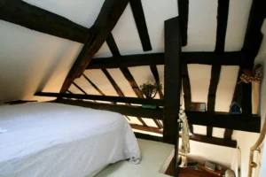 Chambre en mezzanine sous les poutres apparentes d’un loft à Paris 2, offrant un espace nuit intime et chaleureux dans le quartier Montorgueil.