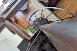 Vue plongeante sur l’escalier en métal d’un loft à vendre à Paris 18, quartier Marx Dormoy – Marché de l’Olive, reliant le salon à la mezzanine.