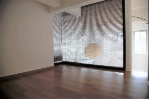 Pièce lumineuse d’un loft à Paris 19, Villa Marcel Lods, séparée par une verrière avec stores vénitiens et parquet en bois clair.