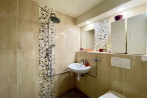 Salle d’eau moderne de l’appartement au château de Villers-sur-Mer, avec douche à l’italienne, carrelage beige et mosaïque de galets pour une ambiance naturelle et élégante.