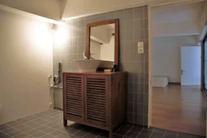 Salle d’eau d’un loft à Paris 19, Villa Marcel Lods, avec meuble vasque en bois, carrelage gris et ouverture vers la chambre.