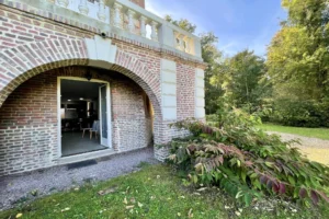 Entrée principale de l’appartement au château de Villers-sur-Mer, sous arcade en briques avec porte vitrée ouvrant sur le parc arboré du Calvados.