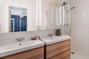 Salle de bains moderne avec double vasque, douche à l’italienne et carrelage blanc texturé, Paris 10 – Gare de l’Est.