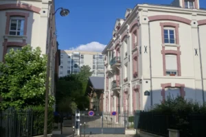 Entrée pavée de la Villa Marcel Lods à Paris 19, dans le quartier des Buttes Chaumont, bordée d’immeubles anciens en briques et d’ateliers rénovés.