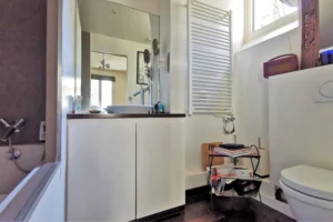 Salle de bains d’un loft à vendre à Paris 18, secteur Marx Dormoy – Marché de l’Olive, avec vasque, miroir et fenêtre sur cour.