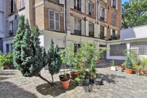 Cour intérieure verdoyante d’un immeuble à Paris 18, quartier Marx Dormoy – Marché de l’Olive, avec plantes en pots et façades typiques.