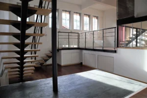 Escalier en métal et bois d’un loft situé Villa Marcel Lods à Paris 19, reliant la mezzanine vitrée au niveau principal dans un espace lumineux et contemporain.