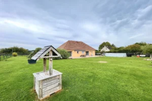 Vue dégagée sur la maison familiale de plain-pied à Le Torquesne 14130, avec grand jardin clos, pelouse entretenue et puits décoratif typique du Calvados.