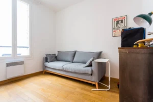 Pièce lumineuse avec parquet en bois et canapé gris, idéale pour bureau ou chambre – appartement Paris 9 Saint-Georges