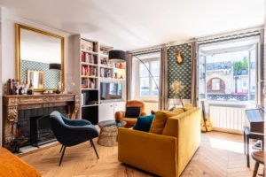 Salon élégant avec cheminée ancienne, bibliothèque intégrée et parquet en chevron, proche de la Gare de l’Est à Paris 10.