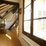 Fenêtre en bois laissant entrer la lumière naturelle dans un loft parisien avec parquet et poutres apparentes, situé à Paris 2 Montorgueil.