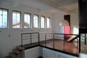 Mezzanine lumineuse d’un loft à Paris 19, Villa Marcel Lods, avec garde-corps en métal et parquet en bois, baignée de lumière naturelle grâce aux grandes fenêtres.