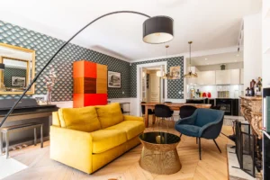 Salon avec canapé jaune et cuisine ouverte contemporaine, espace traversant lumineux près de la Gare de l’Est à Paris 10.