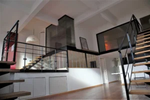 Espace de vie d’un loft d’architecte à Paris 19, Villa Marcel Lods, avec escalier métallique, verrière intérieure et volumes ouverts sur deux niveaux.
