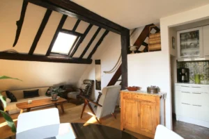 Séjour sous combles avec poutres apparentes et coin cuisine, ambiance chaleureuse typique des lofts du quartier Étienne Marcel à Paris 2.