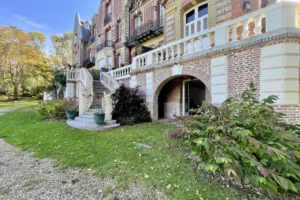 Escalier d’accès en pierre et entrée voûtée du château de Villers-sur-Mer, entourés de végétation et d’éléments architecturaux en briques et pierres typiques du Calvados.