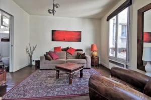 Salon d’un appartement loft à vendre à Paris 18, Marché de l’Olive, décoré dans un style chaleureux avec canapé, fauteuils en cuir et grande fenêtre sur cour.