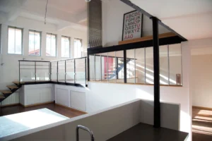 Verrière intérieure de style industriel dans un loft à Paris 19, Villa Marcel Lods, mêlant métal noir et lumière naturelle sur parquet en bois.