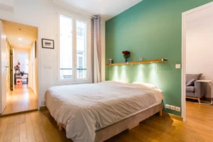 Chambre parentale lumineuse avec mur vert, lit double et parquet en bois – appartement Paris 9 Saint-Georges