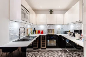 Cuisine équipée contemporaine avec façades laquées blanches, électroménager intégré et sol graphique, Paris 10 – Gare de l’Est.