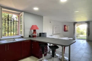 Cuisine ouverte sur le séjour lumineux de l’appartement au château de Villers-sur-Mer, avec vue sur le jardin et éléments décoratifs aux tons rouges et gris.