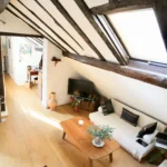 Salon sous combles avec parquet et poutres apparentes, éclairé par un velux, typique d’un loft parisien du quartier Montorgueil à Paris 2.