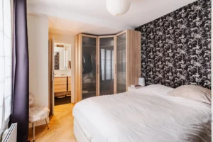 Chambre parentale avec grand dressing d’angle, papier peint tropical noir et blanc et accès direct à la salle d’eau, Paris 10 – Gare de l’Est.