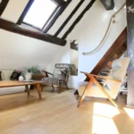 Coin salon chaleureux sous combles avec velux, poutres apparentes et parquet en bois, dans un appartement de charme à Paris 2 Montorgueil.