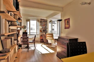 Séjour lumineux d’un appartement 2 pièces rue Poissonnière Paris 2, avec bibliothèque murale, parquet clair et grandes fenêtres donnant sur cour.
