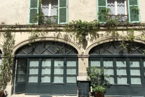 Façade d’un immeuble parisien du passage Delanos, avec grandes fenêtres en arche, volets verts et plantes grimpantes caractéristiques du quartier Faubourg Saint-Denis.