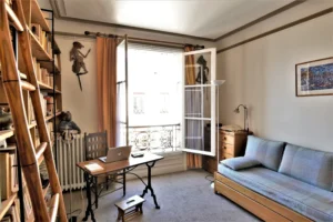 Chambre-bureau lumineuse d’un duplex rue du Faubourg Saint-Denis, avec grande bibliothèque, bureau en bois, canapé-lit et fenêtre ouvrant sur cour dans le 10ᵉ arrondissement.