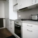 Cuisine équipée d’un appartement situé rue du Faubourg Saint-Denis à Paris 10, avec nombreux rangements, four encastré, plaque de cuisson et plan de travail moderne.