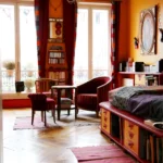 Séjour lumineux avec grandes fenêtres donnant sur balcon, parquet en point de Hongrie, coin salon avec fauteuils et lit intégré dans un appartement situé rue du Faubourg Saint-Denis à Paris 10.