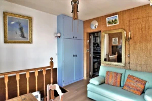 Espace salon à l’étage d’un duplex rue du Faubourg Saint-Denis, avec canapé vert, grand miroir doré, rangements bleus et accès vers la mezzanine.