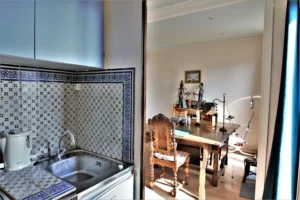 Petit espace cuisine carrelé en bleu et blanc donnant sur une salle à manger lumineuse avec mobilier ancien dans un duplex situé rue du Faubourg Saint-Denis à Paris 10.