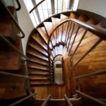 Escalier ancien en bois massif d’un immeuble situé rue du Faubourg Saint-Denis à Paris 10, photographié en plongée avec lumière naturelle venant de la grande fenêtre.