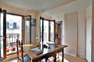 Salle à manger lumineuse d’un duplex rue du Faubourg Saint-Denis, avec table en bois, grandes fenêtres ouvertes et vue dégagée sur les toits du 10ᵉ arrondissement.